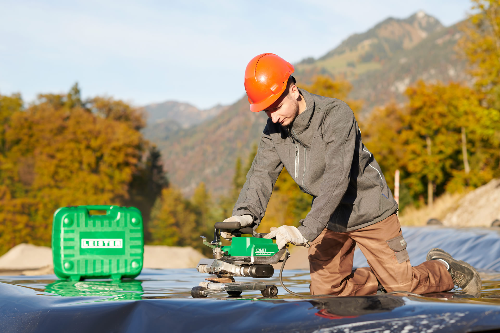 Trabajador utilizando la soldadora automática Leister COMET 700 en instalación de geomembranas en terreno irregular