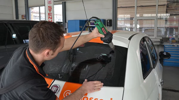 Técnico utilizando soplador manual Leister para secar y reparar detalles en un automóvil durante el proceso de mantenimiento