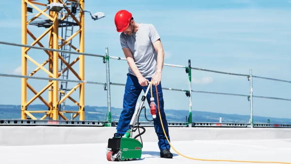 Trabajador soldando membrana TPO en techo plano con máquina automática Leister VARIMAT V2, garantizando uniones seguras y resistentes