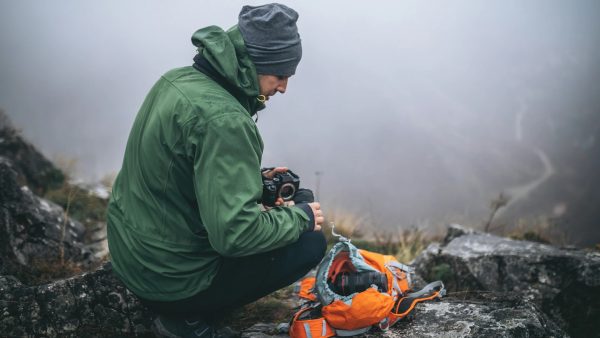 Persona con campera verde y mochila impermeable soldada, en ambiente de montaña con neblina
