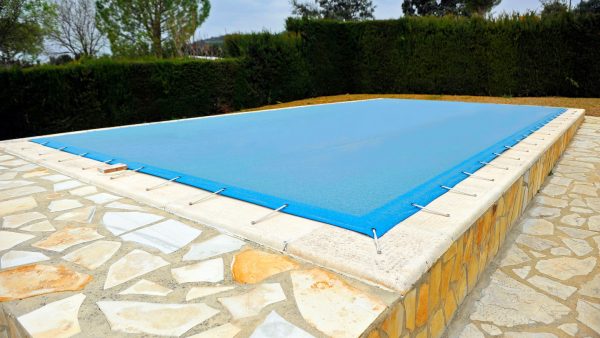 Cobertura plástica soldada de color azul protegiendo una piscina residencial al aire libre