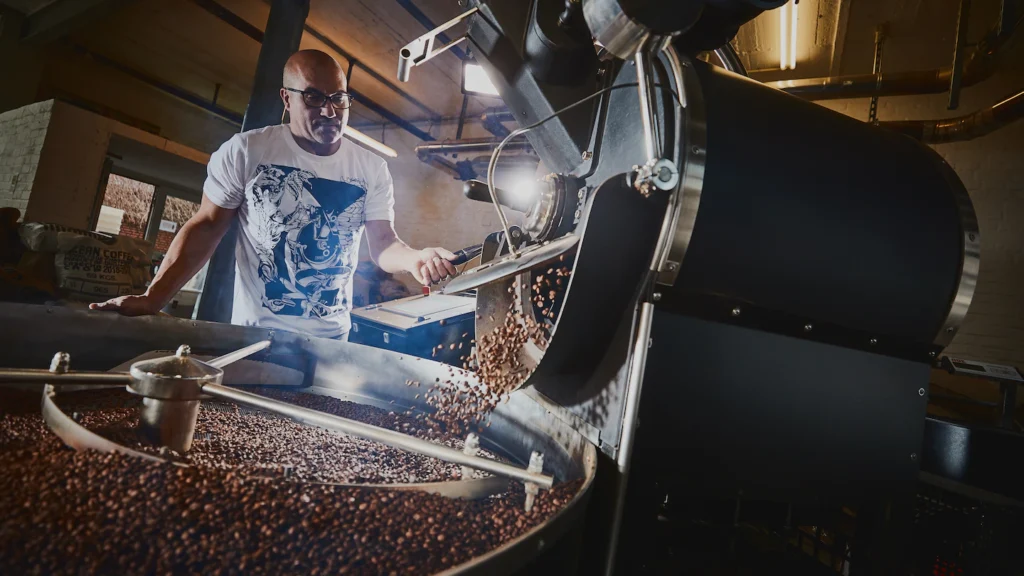 Operario supervisando el proceso de torrefacción de granos de café en tambor con una máquina PROBAT
