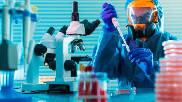 Científico en laboratorio con ropa de protección química soldada, trabajando con material biológico