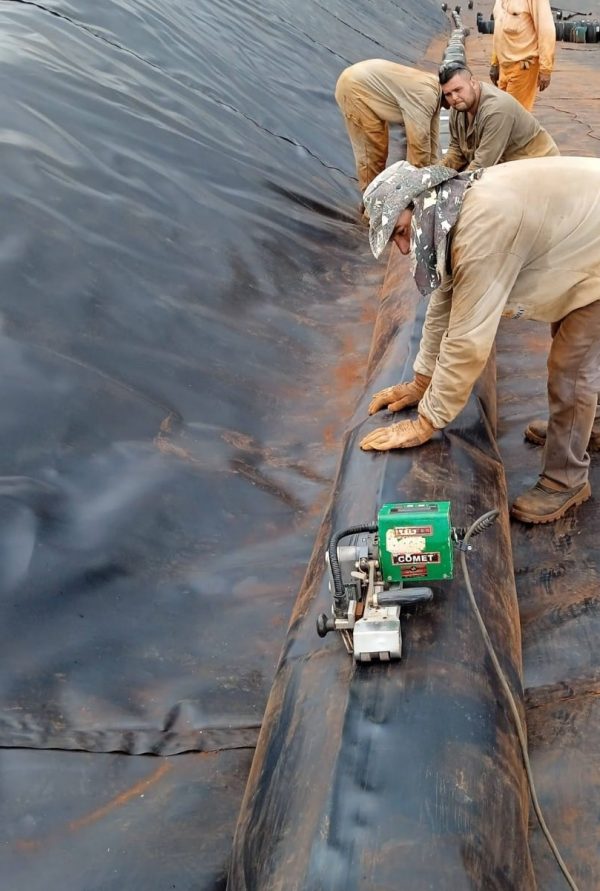 Instaladores realizando soldadura de geomembrana PEAD con máquina automática Leister COMET en una laguna de gran tamaño, garantizando estanqueidad y precisión