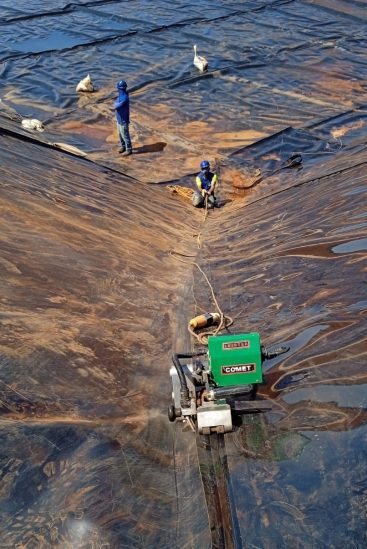 Operarios soldando geomembranas en una rampa inclinada con máquina automática Leister COMET, garantizando una unión segura en pendientes pronunciadas