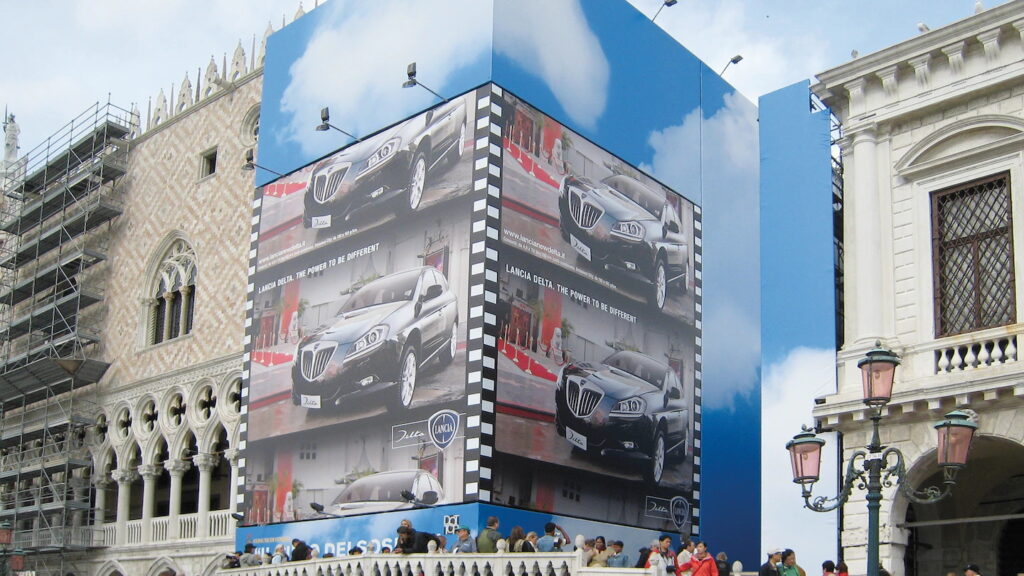 Outdoor publicitario de gran formato soldado con máquinas automáticas y sopladores de aire caliente Leister, mostrando la aplicación de lonas de PVC resistentes al viento y a la intemperie en fachadas para campañas de marketing visual