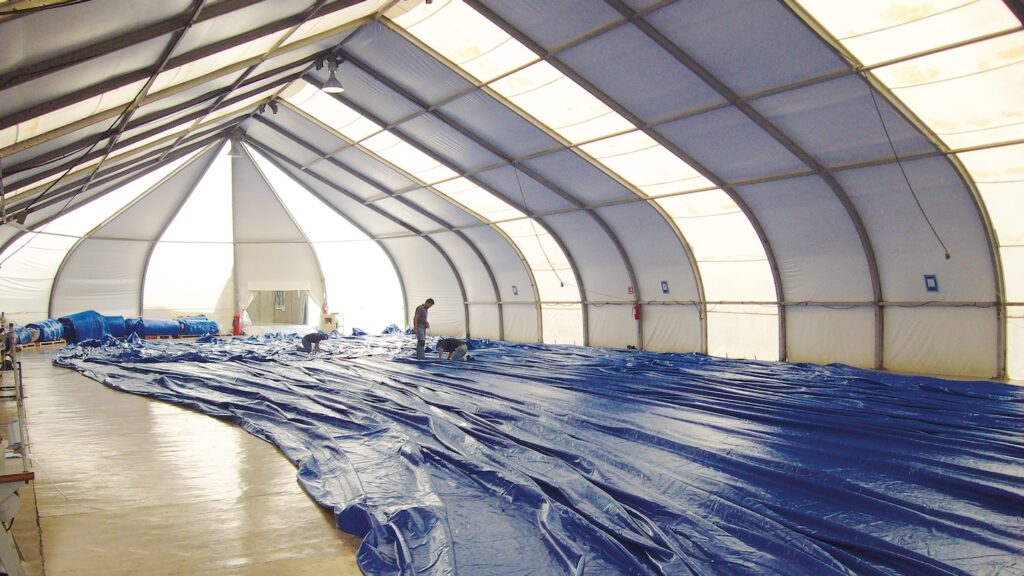 Vista interior de una carpa en montaje, con lona extendida en el suelo y proceso de soldadura realizado con equipos Leister