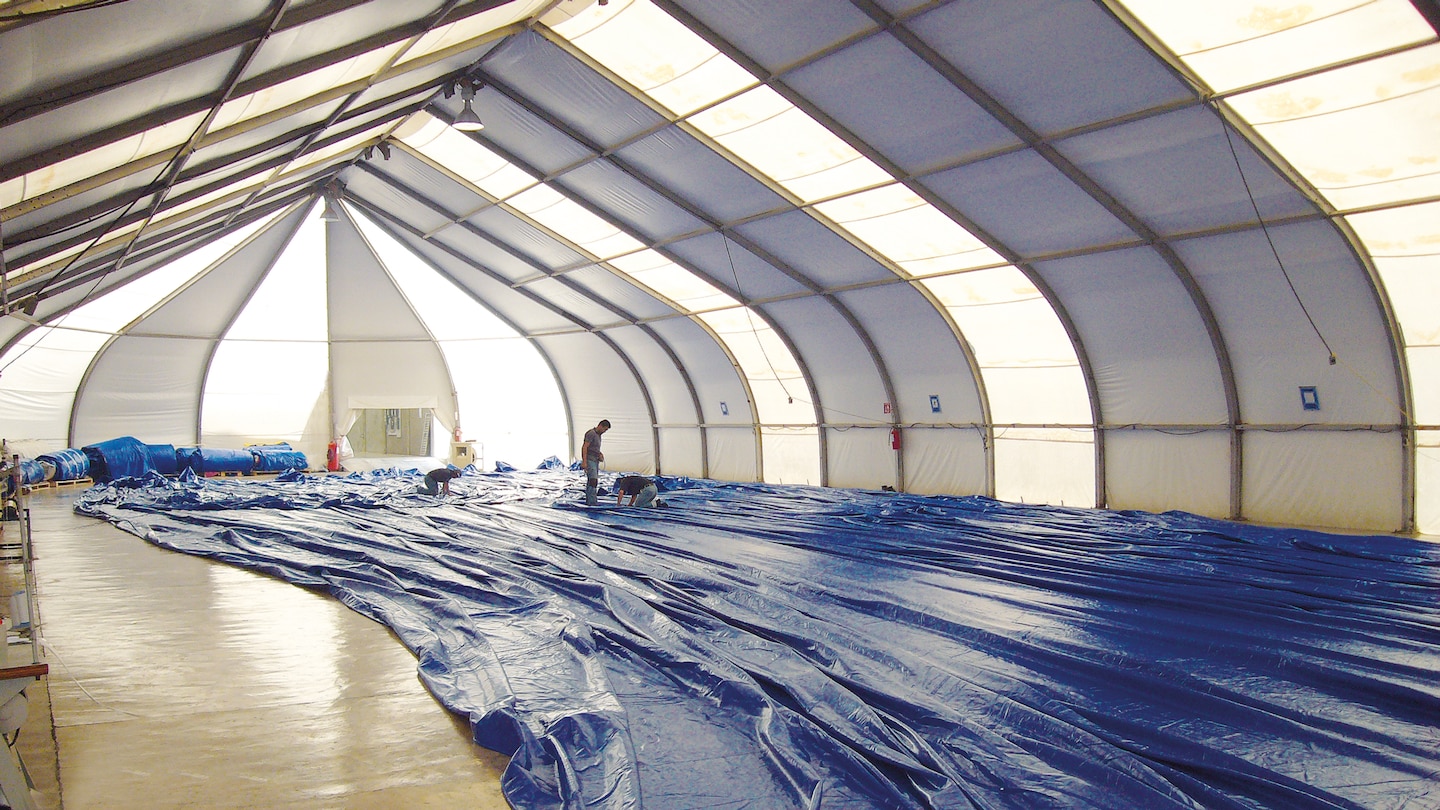 Vista interior de una carpa en montaje, con lona extendida en el suelo y proceso de soldadura realizado con equipos Leister