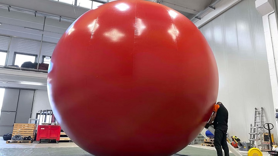 Obra inflável gigante em formato de esfera vermelha sendo inspecionada por técnico da Nasoallinsù, soldada com tecnologia Leister SEAMTEK W-2000 AT