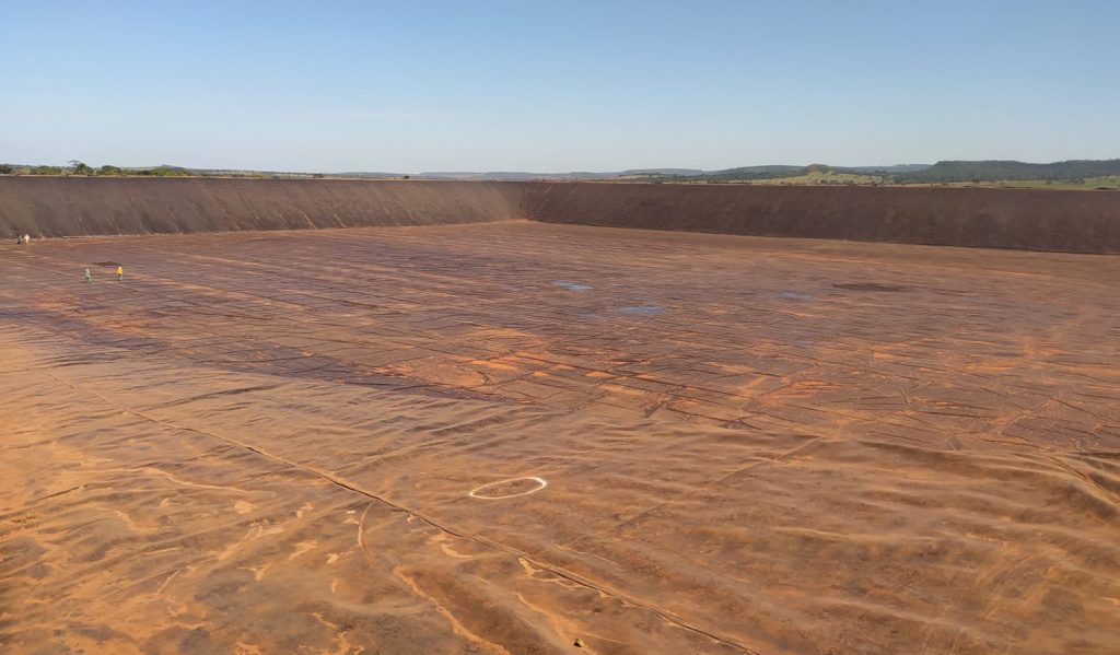 Instalación de geomembrana PEAD en una laguna artificial para almacenamiento de agua, mostrando el avance del revestimiento completo antes del llenado final