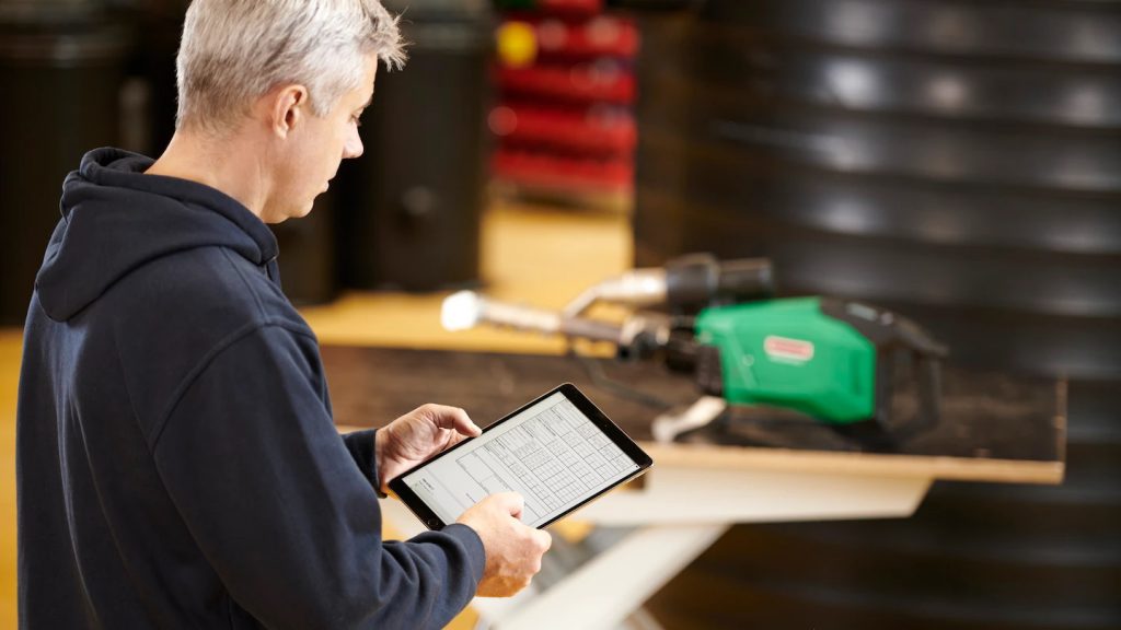 Engenheiro analisa registros de soldagem em um tablet enquanto extrusora de solda Leister WELDPLAST 600 está posicionada para operação em fábrica de tanques plásticos