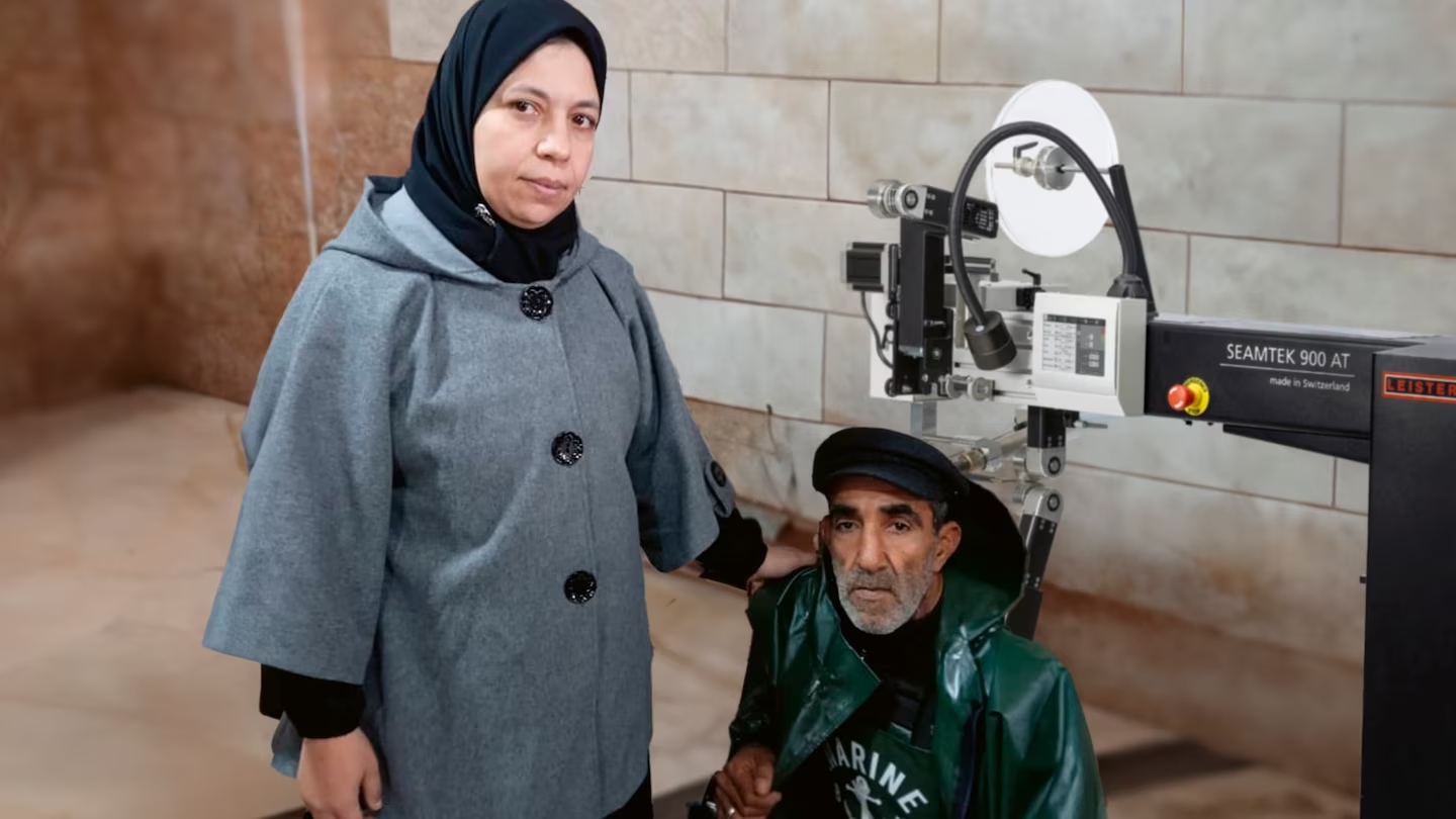 Pareja argelina junto a la máquina de soldadura Leister SEAMTEK 900 AT, mostrando uniformes de trabajo para pescadores