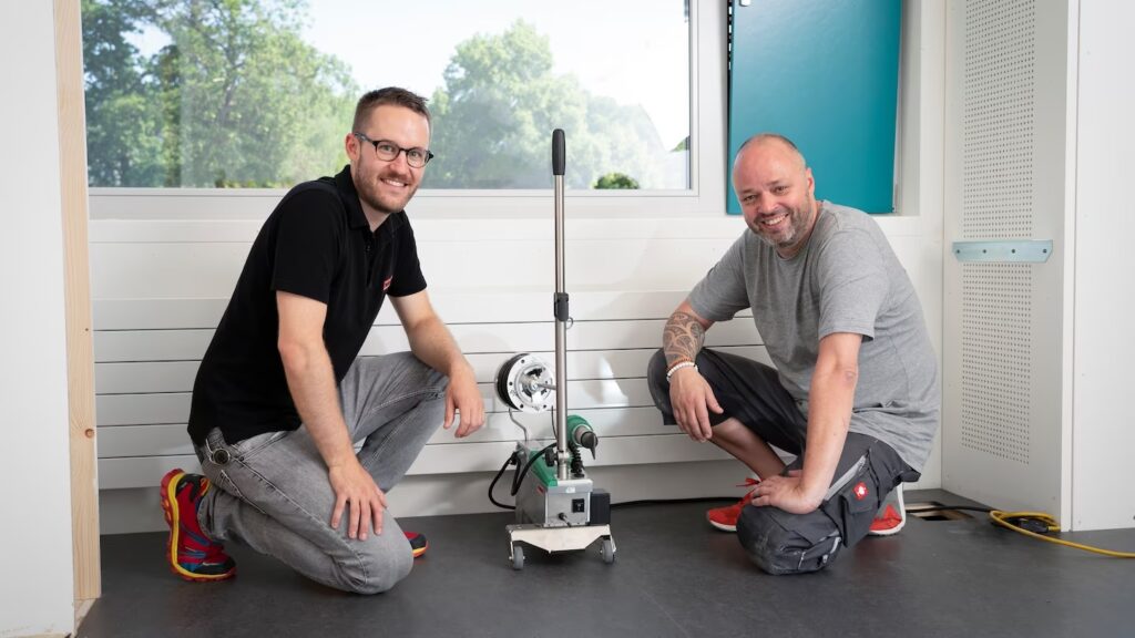 Instaladores de pisos suizos junto a la máquina Leister UNIFLOOR durante el proyecto de instalación en una escuela de Zúrich