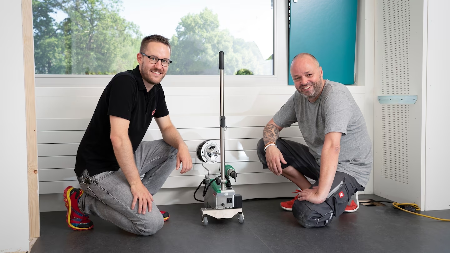 Instaladores de pisos suizos junto a la máquina Leister UNIFLOOR durante el proyecto de instalación en una escuela de Zúrich