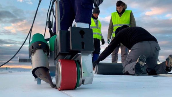 Equipo Leister UNIROOF trabajando en la impermeabilización de un techo plano mientras el equipo de instaladores supervisa el proceso