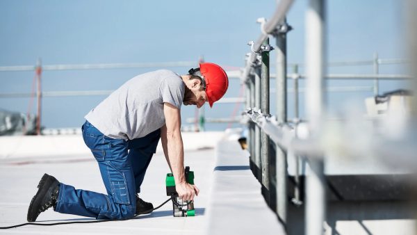 Instalador arrodillado utilizando la soldadora semiautomática Leister UNIDRIVE 500 para unir membranas en la impermeabilización de un techo plano