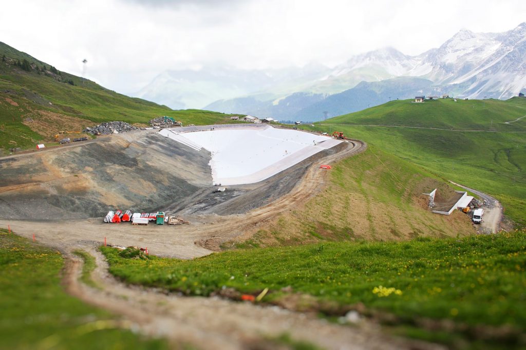 Vista ampla de reservatório revestido com geomembrana em área montanhosa; solução de retenção hídrica aplicada com suporte de soldagem Leister