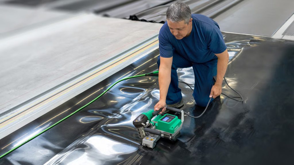 Operario soldando geomembrana con la soldadora automática Leister TWINNY en obra, asegurando una costura continua y uniforme