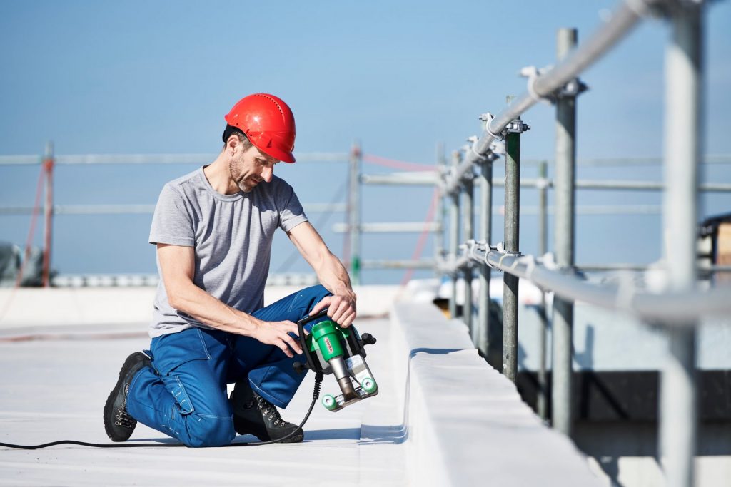 Techador soldando membrana termoplástica en techo plano con la soldadora semiautomática de aire caliente Leister UNIDRIVE 500