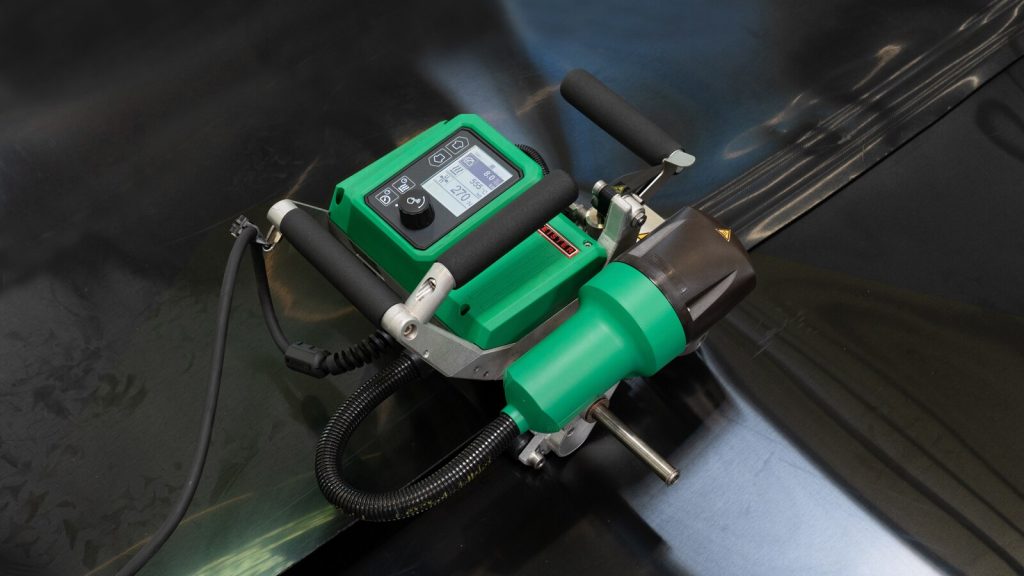 Leister TWINNY T7 trabajando sobre geomembrana oscura, con display digital visible que registra parámetros de soldadura para control de calidad