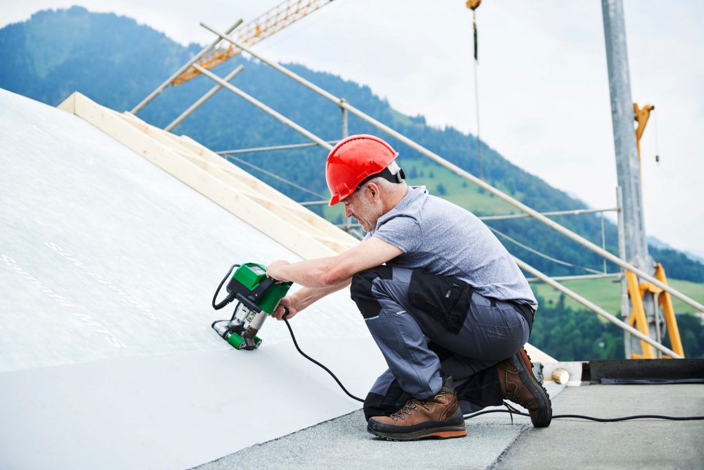 Operario soldando membrana en techo inclinado con Leister UNIDRIVE 500 durante trabajos de impermeabilización
