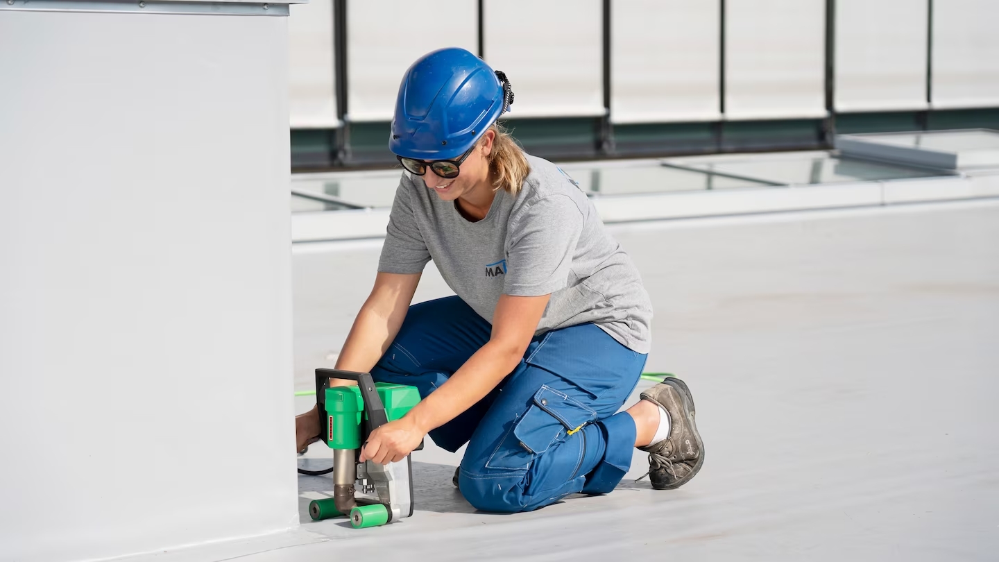 Técnica usando la Leister UNIDRIVE 500 para soldar una membrana junto a una pared, con manejo ergonómico y preciso