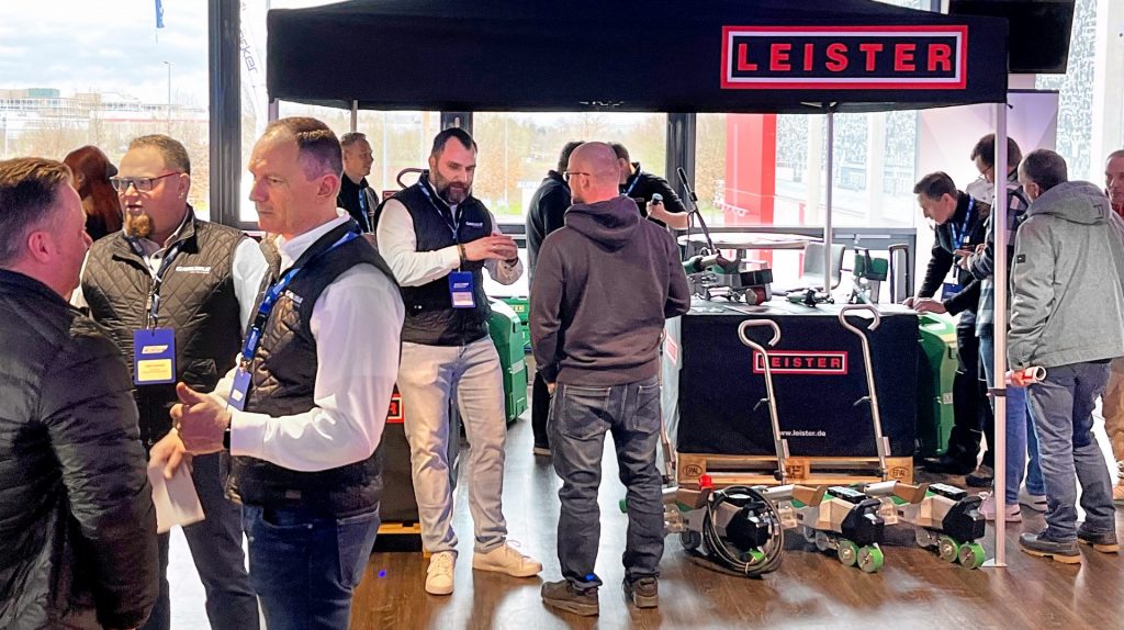Stand de Leister en el evento de Carlisle: visitantes conversando y observando las soldadoras automáticas VARIMAT expuestas, en un área de demostración bajo marquesina Leister