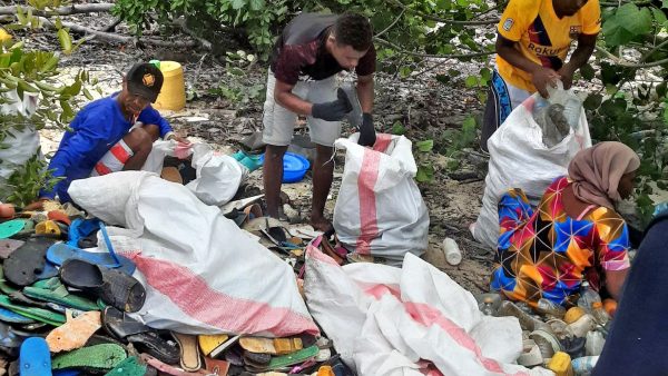 Personas recolectando residuos plásticos y ojotas en una playa de Kenia durante una limpieza costera apoyada por Leister