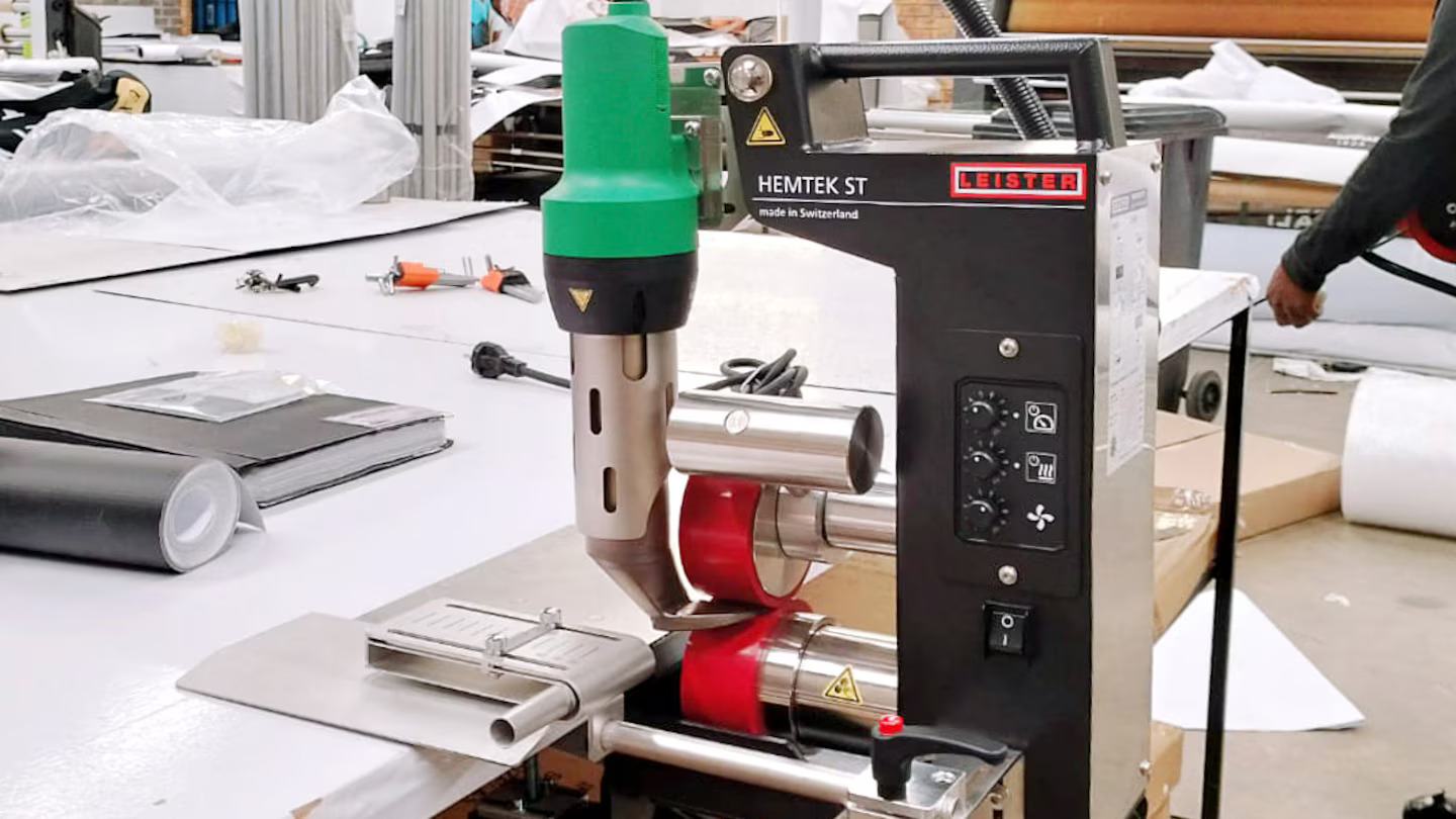 Máquina dobladilladora Leister HEMTEK ST realizando dobladillos limpios y uniformes en lona/lámina para aplicaciones de señalización