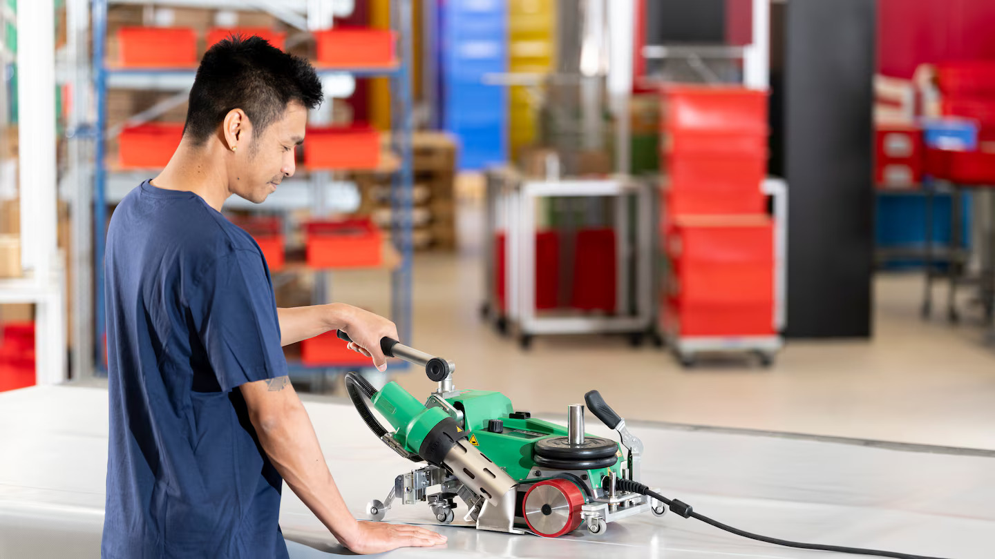 Operador realizando soldadura de lonas sobre mesa utilizando la máquina automática Leister UNIPLAN en un entorno industrial