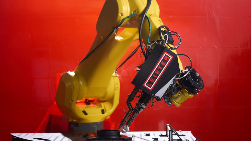 Brazo robótico FANUC equipado con la extrusora Leister WELDPLAST 200-i realizando soldadura por extrusión en una celda automatizada