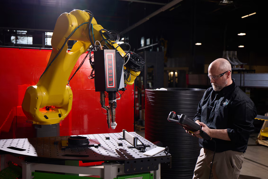Técnico monitoreando el proceso de soldadura robótica mientras el robot FANUC opera con la extrusora Leister WELDPLAST 200-i en el área de producción