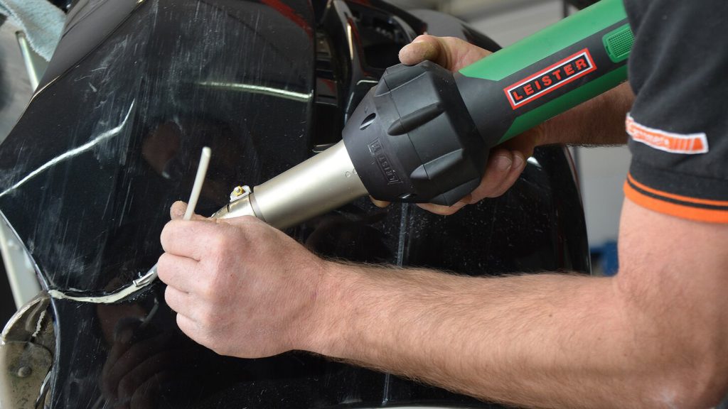 Técnico automotriz utilizando el soplador de aire caliente Leister TRIAC-ST para realizar una reparación de soldadura plástica en un componente de vehículo