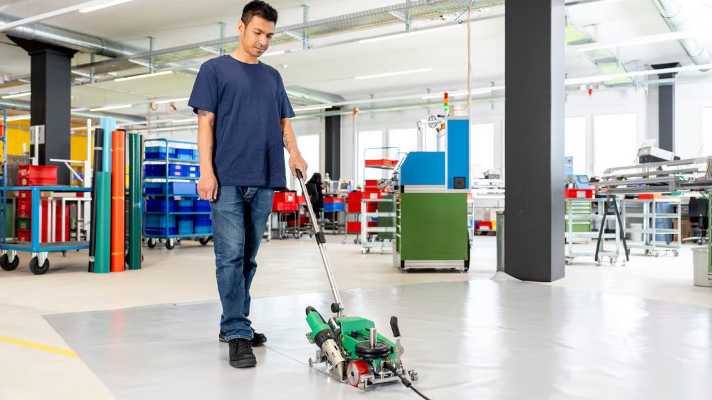 Soldadura eficiente de grandes superficies de lona en el suelo utilizando la Leister UNIPLAN 510 con mango guía para facilitar el manejo.