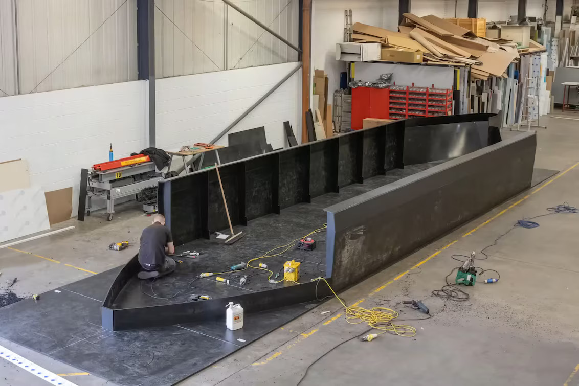 Construcción del casco de un barco de canal en PEAD dentro del taller, con paneles ensamblados y trabajos de soldadura de termoplásticos realizados con herramientas Leister